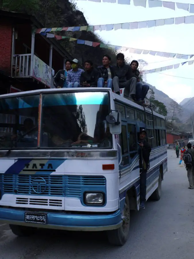 Locals ride the top of the bus through Tatopani in the Kathmandu Valley