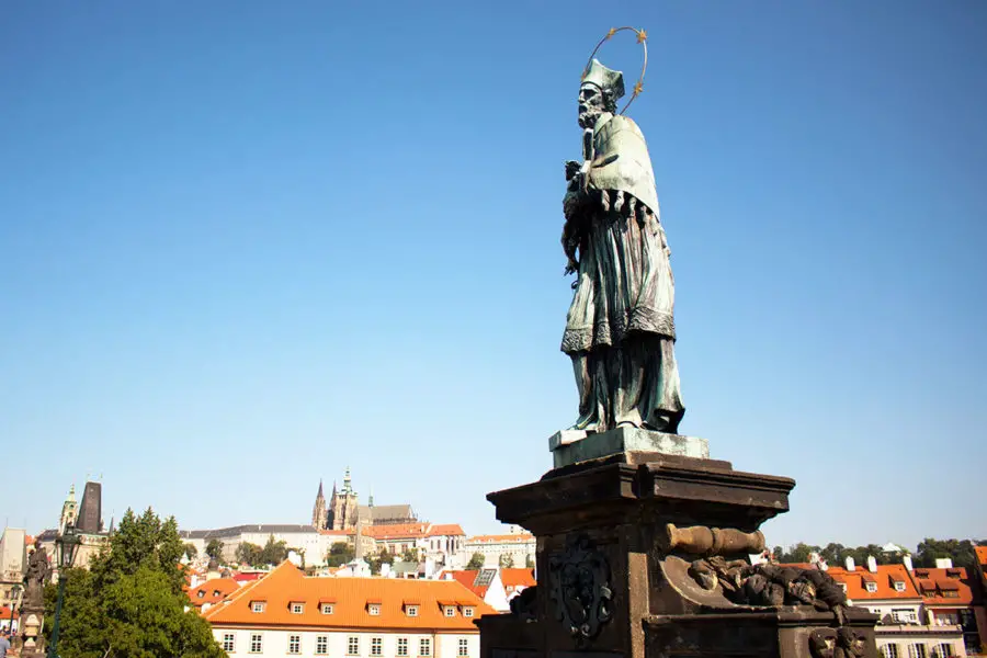 The statue of St. John of Nepomuk on Charles Bridge with Prague castle in the background, one of the Best Free Things To Do In Prague, what to see in Prague, Prague on a budget