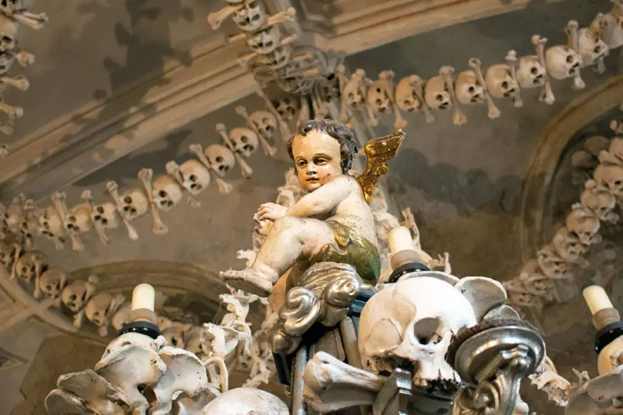 A cheerful cherub sits atop a candelabra of skulls and bones | Sedlec Ossuary